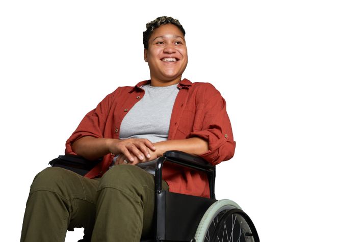 A smiling African woman in a wheelchair, wearing a red shirt over a gray T-shirt and olive green pants.