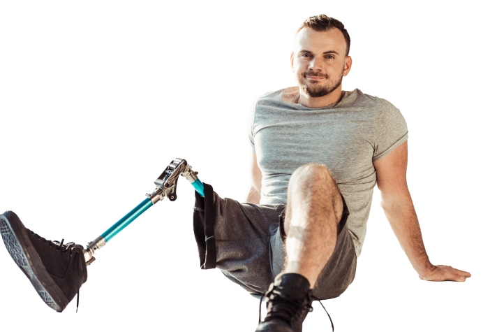 A man with a prosthetic leg, wearing a gray T-shirt and shorts, sitting on the ground and smiling.