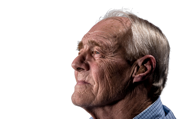 Profile of an elderly man with white hair wearing a hearing aid, looking thoughtful.