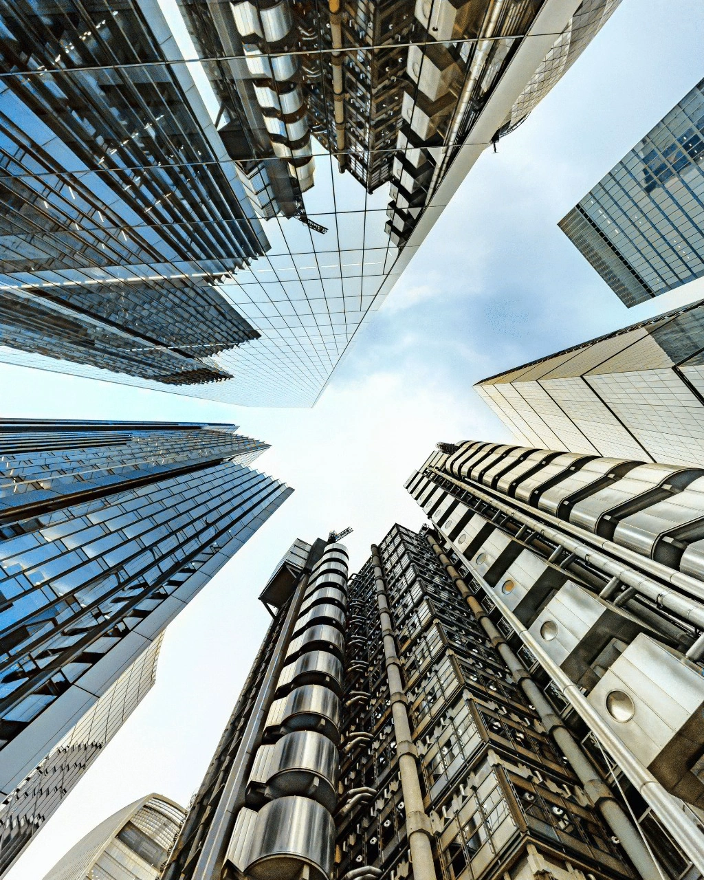 Looking up at tall skyscrapers against a cloudy sky in an urban area, showcasing architectural symmetry.