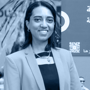 A woman in formal wear, including a blazer and bow tie, is smiling at the camera.