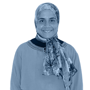 A woman in a long-sleeved top with a decorative neckline and patterned scarf, standing against a white background.